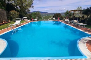 Une piscine rectangulaire à l’eau d’un bleu limpide, entourée de chaises longues blanches et d’une pergola en bois.