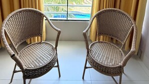 Ein Zimmer mit zwei Korbstühlen, die vor ein großes Fenster mit Vorhängen blicken.