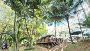 Eine Holzterrasse mit einer Treppe zu einer überdachten Sitzgruppe, umgeben von üppiger Vegetation und Palmen.