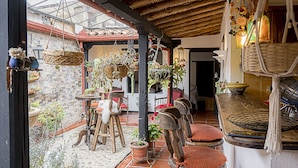 A rustic outdoor seating area with wooden chairs and tables, surrounded by potted plants and hanging baskets.