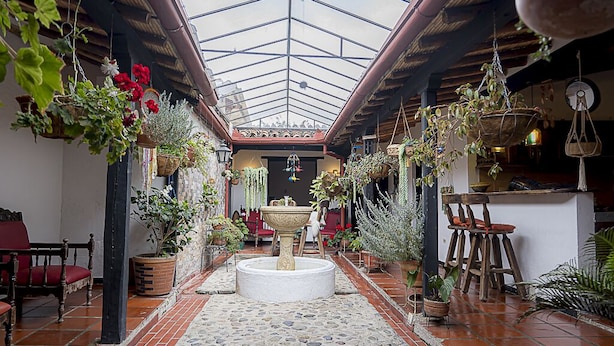A spacious atrium with a high ceiling, stone flooring, and various potted plants and hanging baskets.