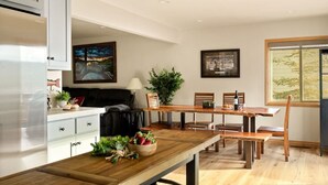 Una cocina moderna con armarios blancos, un comedor con mesas y sillas de madera, y un ventanal con vista a bambú.