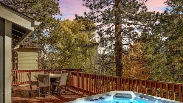 Un jacuzzi en una terraza de madera con una mesa y sillas, rodeado de árboles.