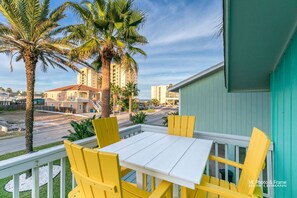 A balcony with yellow chairs and a white table, overlooking a street with palm trees and buildings.