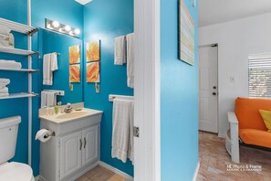 A bathroom with a blue wall, white sink, and toilet. There are towels hanging on the wall and a white cabinet.