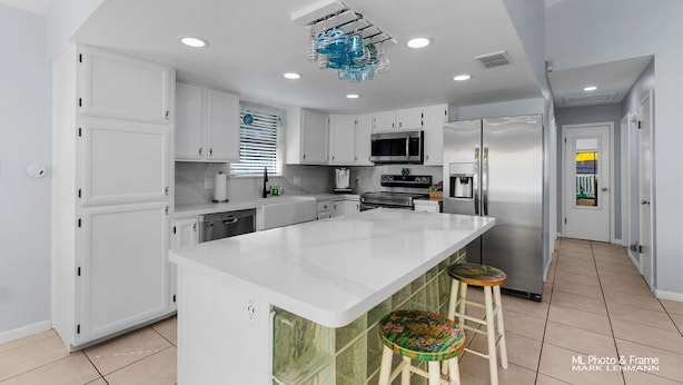Una cocina moderna con armarios blancos, una isla grande, electrodomésticos de acero inoxidable y una lámpara de techo azul distintiva.
