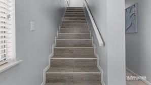 Una escalera con escalones de madera y barandillas blancas, que conduce a un rellano con un interruptor de luz y un pequeño adorno en la pared.
