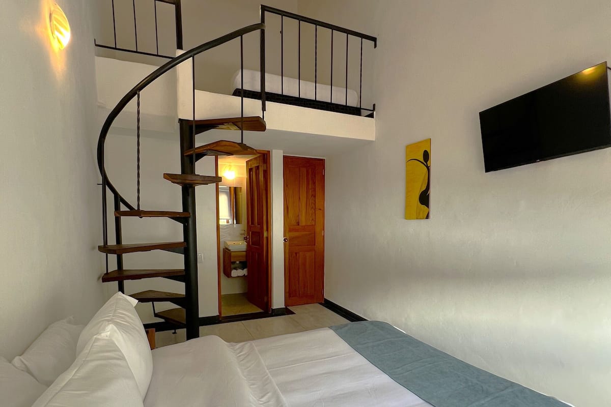 A bedroom with a bed, a staircase, a flat-screen TV, and a wooden door.