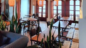 Un vaste espace dédié à la salle à manger, avec des tables et des chaises en bois, des suspensions orange et de grandes fenêtres dotées de cadres en bois.