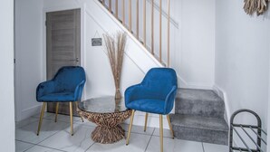 A modern interior with a staircase, two blue chairs, a glass table, and a sign indicating a waiting lounge.