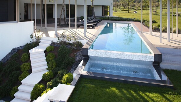 A modern pool with a waterfall feature, surrounded by a well-manicured lawn and a series of white steps leading down to the pool. - Luxury Villa Zio with Pool (Novigrad)