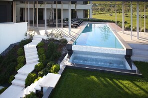 Une piscine moderne agrémentée d’une cascade, entourée d’une pelouse parfaitement entretenue et d’une série de marches blanches descendant vers la piscine.