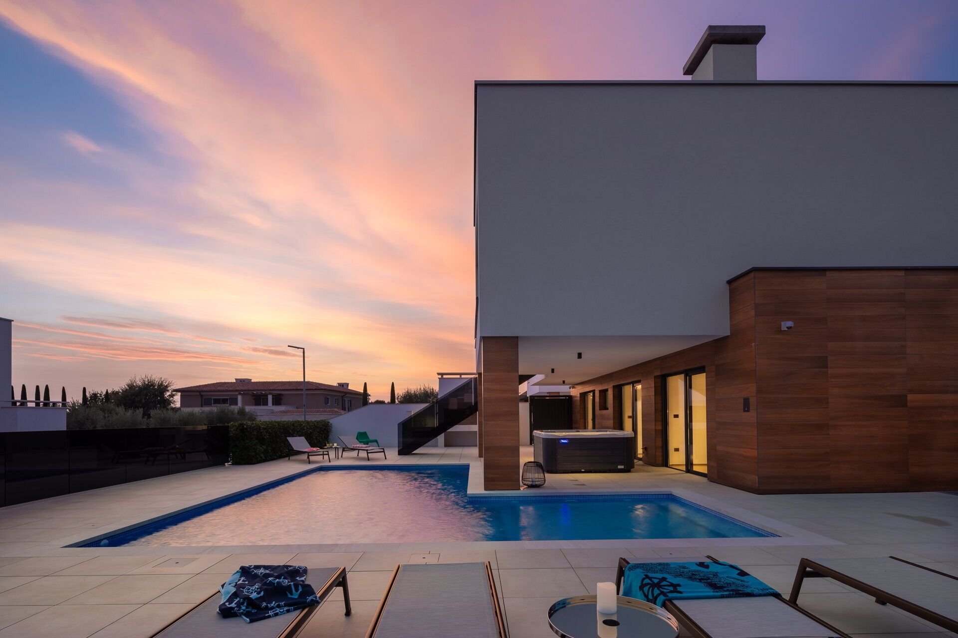 A modern pool area with lounge chairs, a hot tub, and a staircase leading to an upper level.