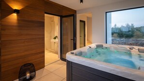 Un baño moderno con pared de madera, cabina de ducha de vidrio, lavamanos blanco y una bañera de hidromasaje con vistas al exterior.