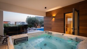 Una piscina interior moderna con un jacuzzi, paredes de paneles de madera y vistas al exterior.