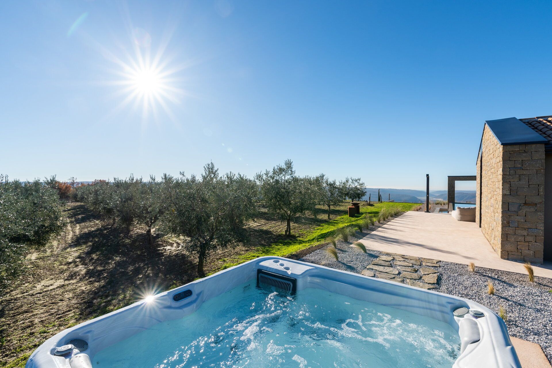 A hot tub with a clear view of an olive grove and a stone building in the background.