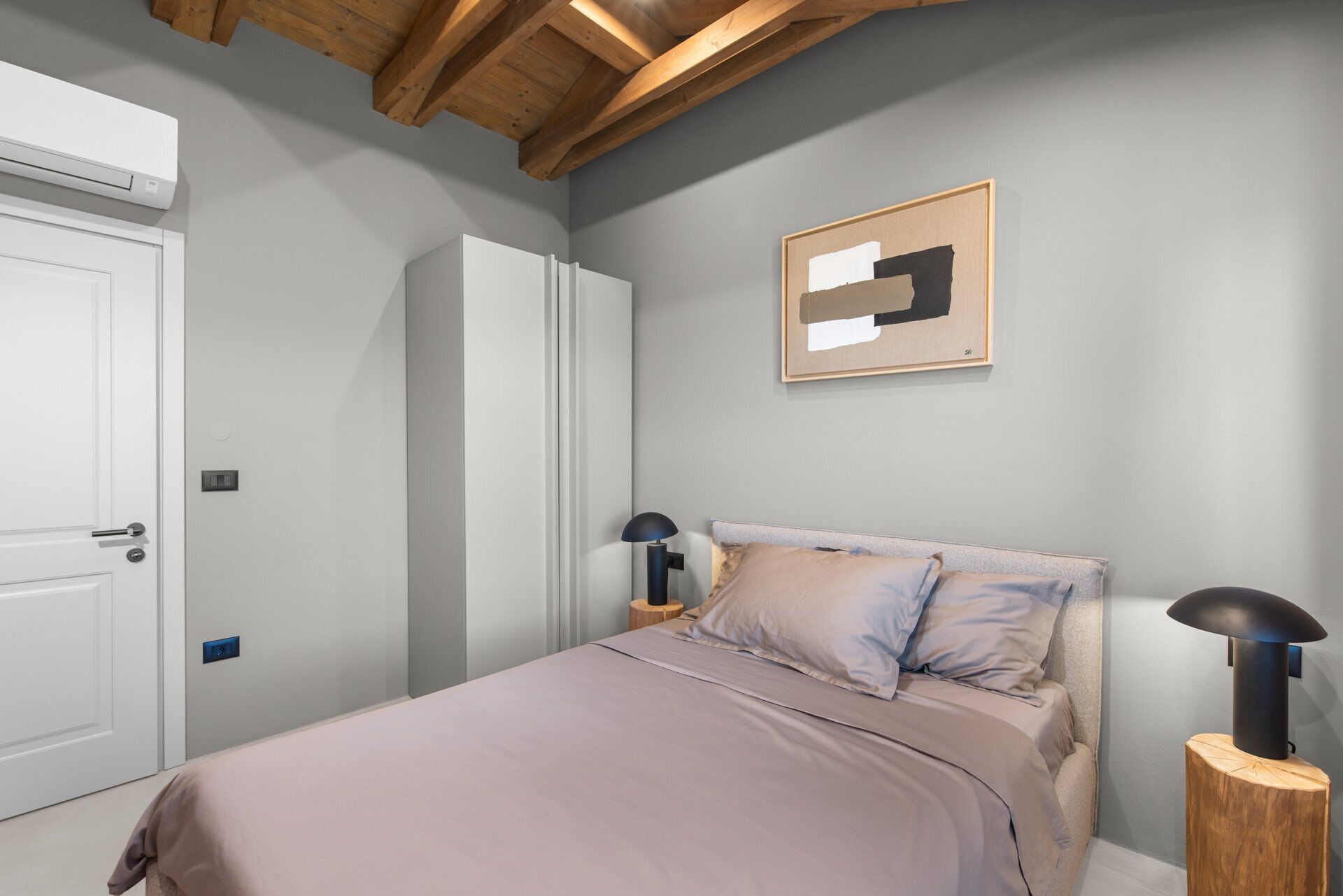 A bedroom with a bed, bedside lamps, a framed abstract artwork, and a wardrobe.