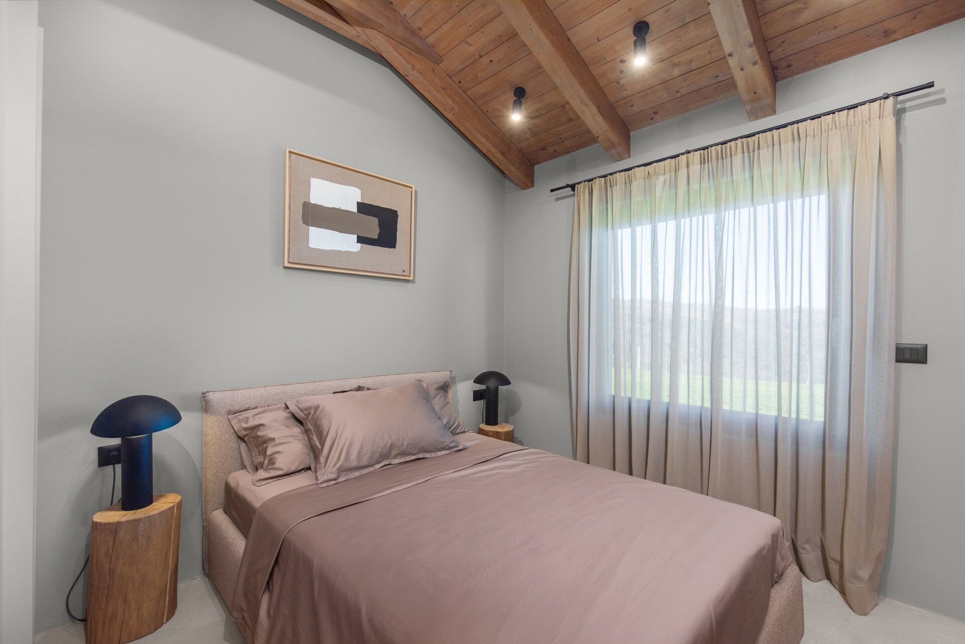 Une chambre à coucher comprenant un lit, une table de chevet, une lampe, un ventilateur de plafond et une fenêtre avec des rideaux.