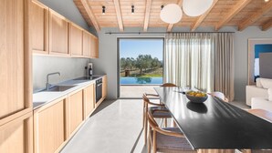 A modern kitchen with wooden cabinets, a black countertop, and a view of a pool and trees. - Villa Vista Verde with Pool (Grožnjan)