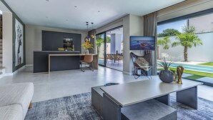 A modern living space with a kitchen, dining area, and a large TV screen. - Luxury Villa Xquisite with Pool (Medulin)