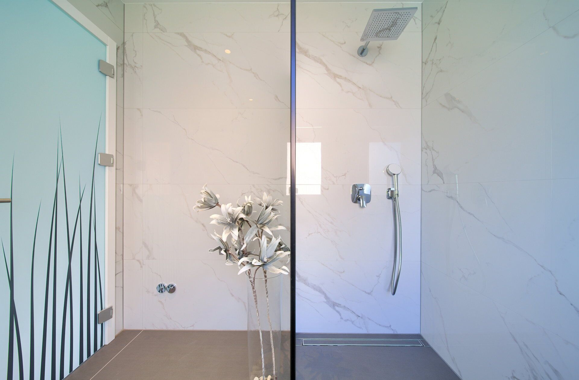 Une salle de bain moderne avec une douche à parois de verre, des murs en marbre et une plante décorative.