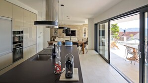 A modern kitchen with a central island, built-in appliances, and a large sliding glass door leading to a balcony. - Villa Hestia with Heated Pool (Lumbarda)