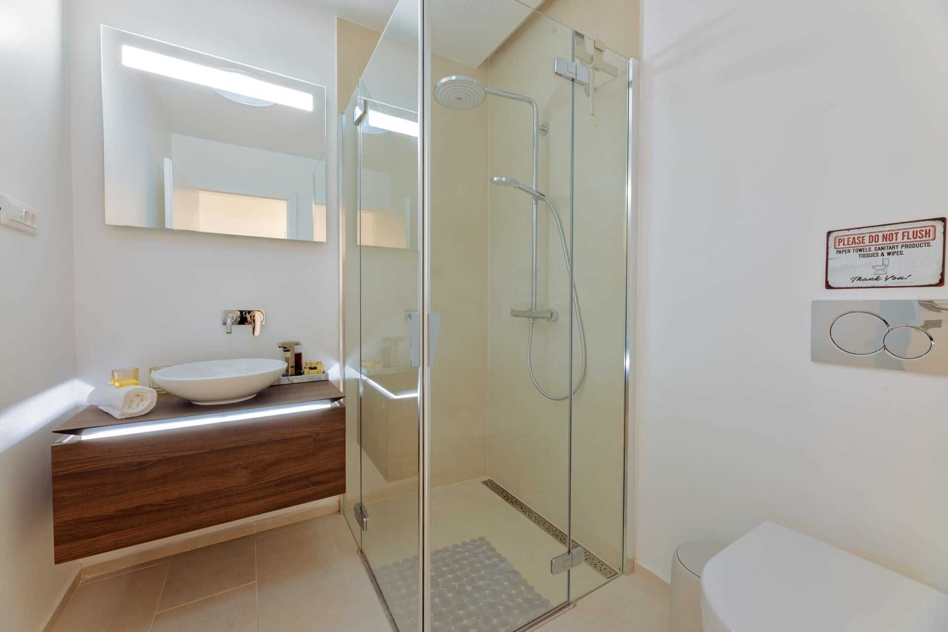A modern bathroom with a glass-enclosed shower, a wooden vanity, and a white sink.