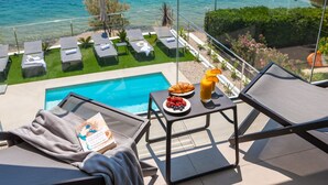 Un espace aménagé au bord de la piscine, avec des chaises longues, une table où sont servis les articles du petit-déjeuner et une vue sur la mer.