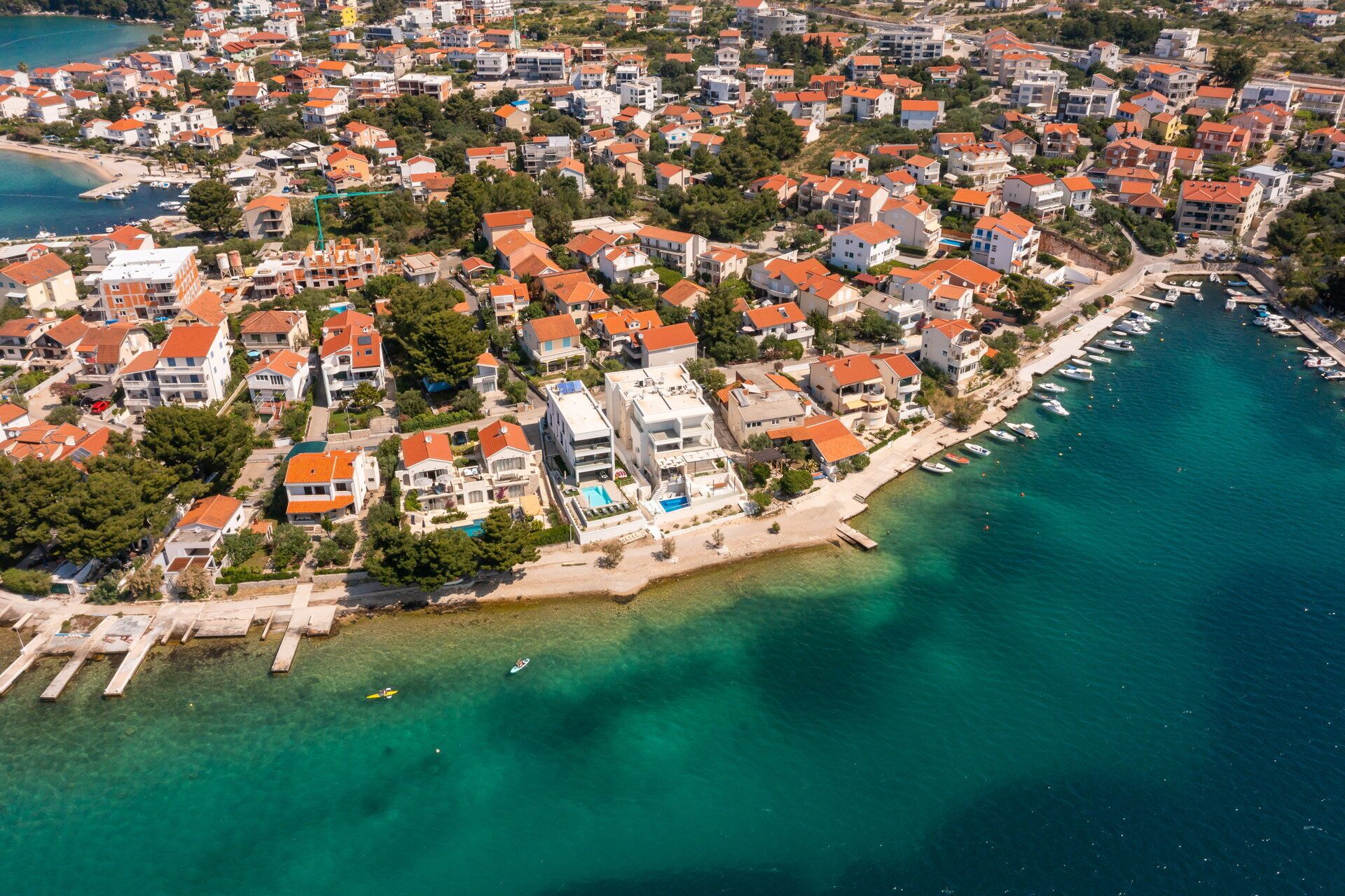 Luftaufnahme einer Küstenwohngegend mit Häusern, Strand und einem Yachthafen.