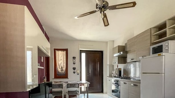 Una cocina moderna con ventilador de techo, un comedor con mesa y sillas, y una sala de estar con sofá y televisor.