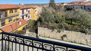 Un balcón con barandilla de hierro forjado que da a una zona residencial con edificios de colores y un cielo azul despejado.