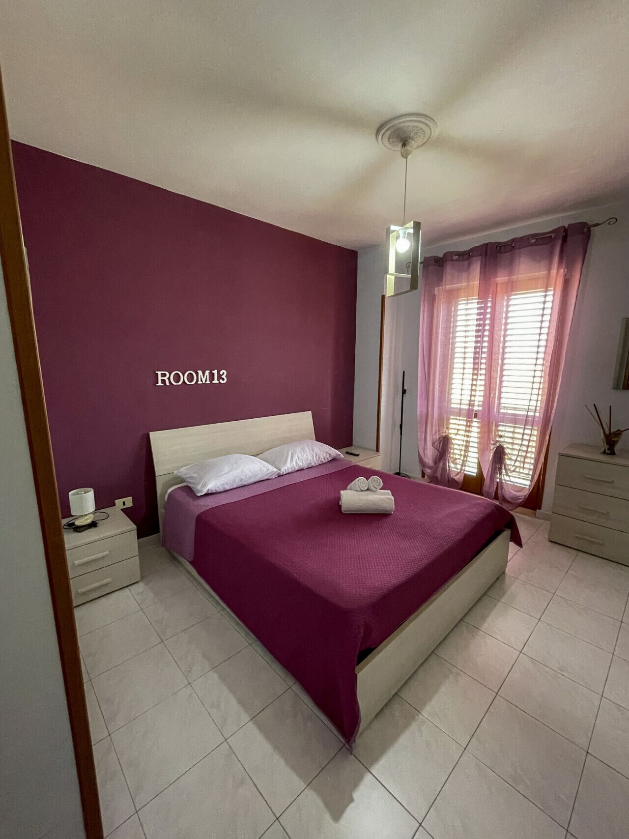 A bedroom with a bed, nightstands, a dresser, and a window with curtains.