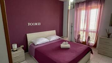 A bedroom with a bed, nightstands, a dresser, and a window with curtains.