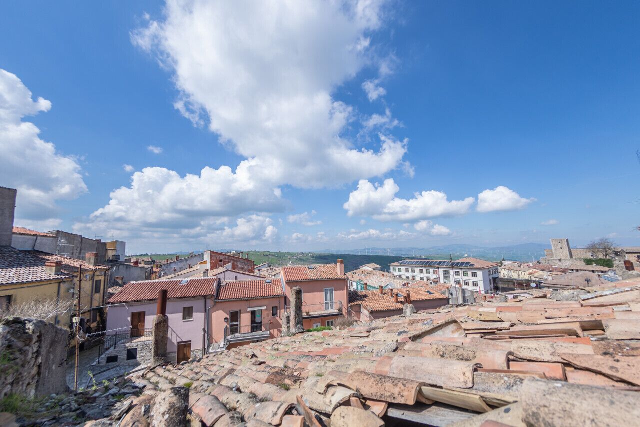 A historic town with terracotta-roofed buildings, cobblestone streets, and a distant view of a castle.