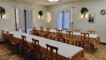 Un salón de conferencias con una larga mesa, sillas de madera, manteles blancos y plantas en macetas.