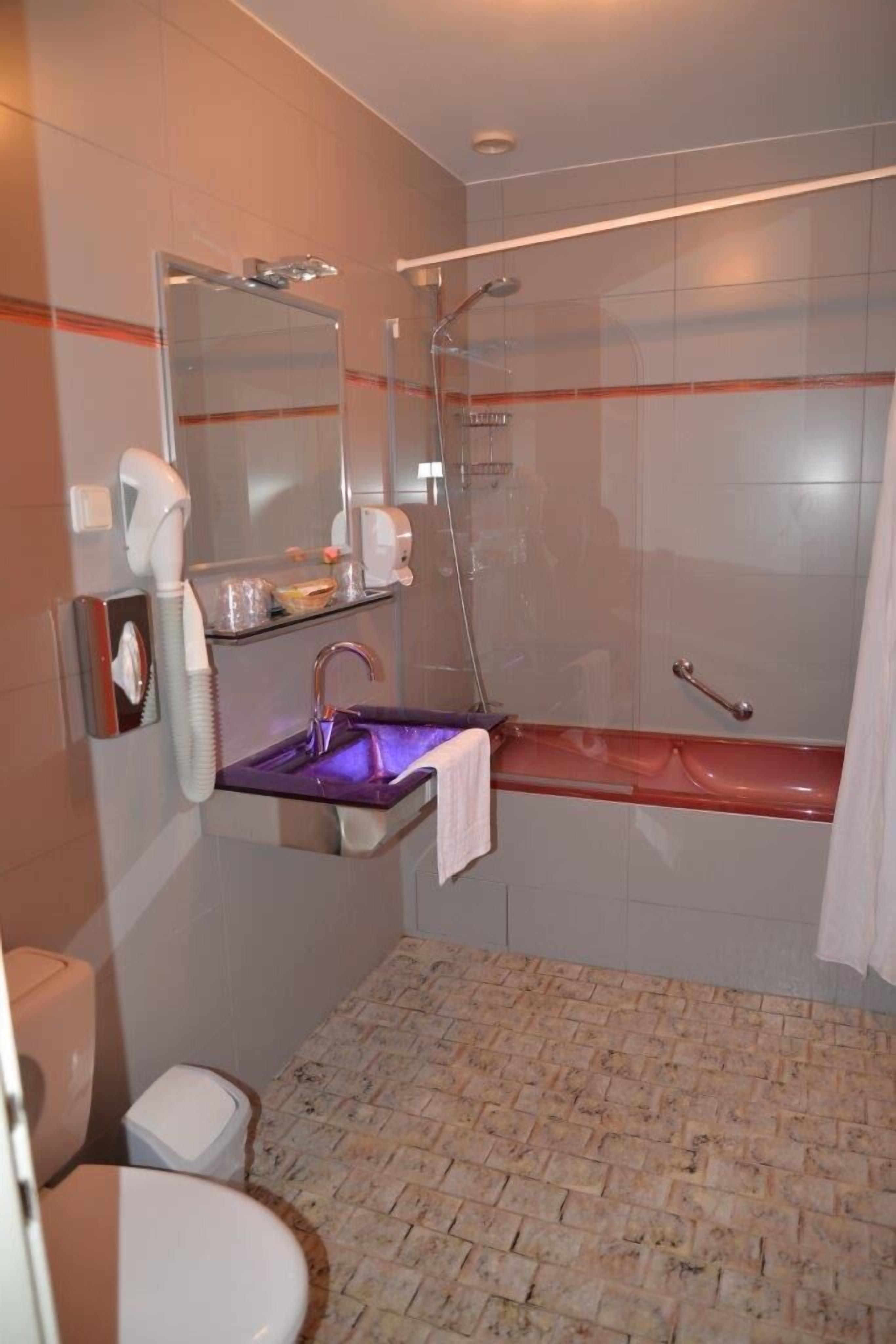 Un baño moderno con cabina de ducha de vidrio, tocador con lavamanos morado y un inodoro blanco.