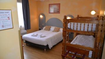 A hotel room with a double bed, a wooden bunk bed, a bedside table, a nightstand, and a wall-mounted lamp.