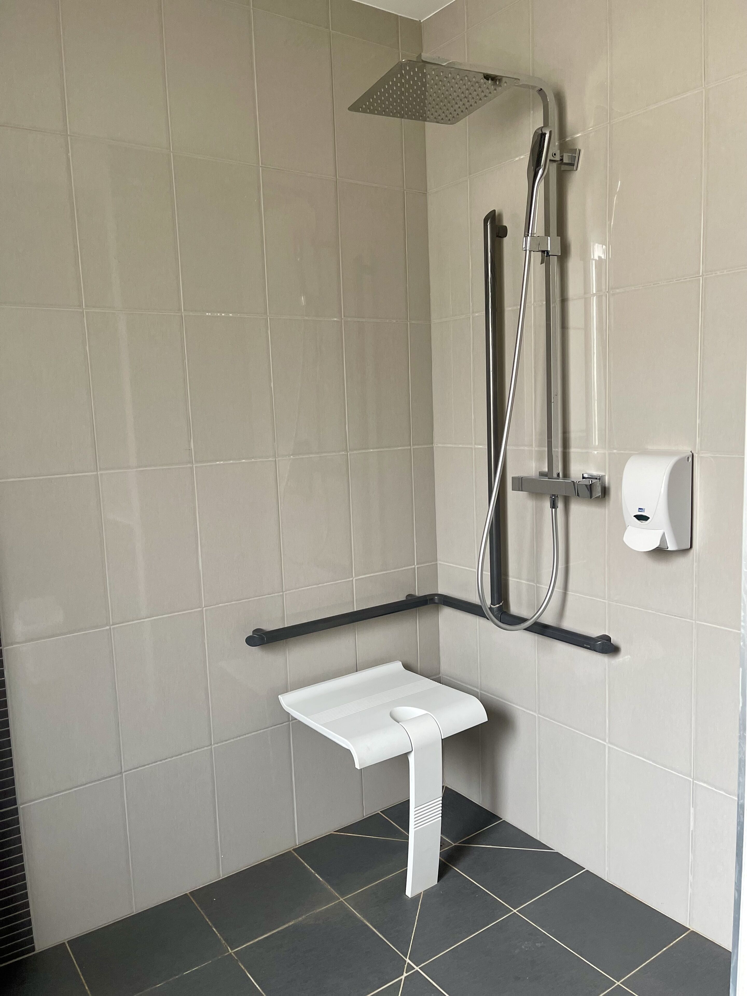Une salle de bain moderne équipée d’une douche, d’un sèche-mains et d’un porte-serviettes blanc.