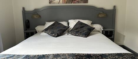 Una cama bien hecha con un edredón estampado oscuro, dos almohadones decorativos y un cuadro de flores colgado en la pared.