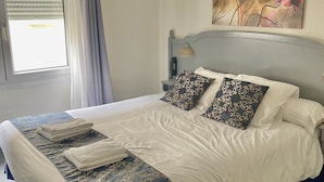 Una cama bien hecha con un edredón azul y blanco, una almohada decorativa y una toalla doblada al lado.