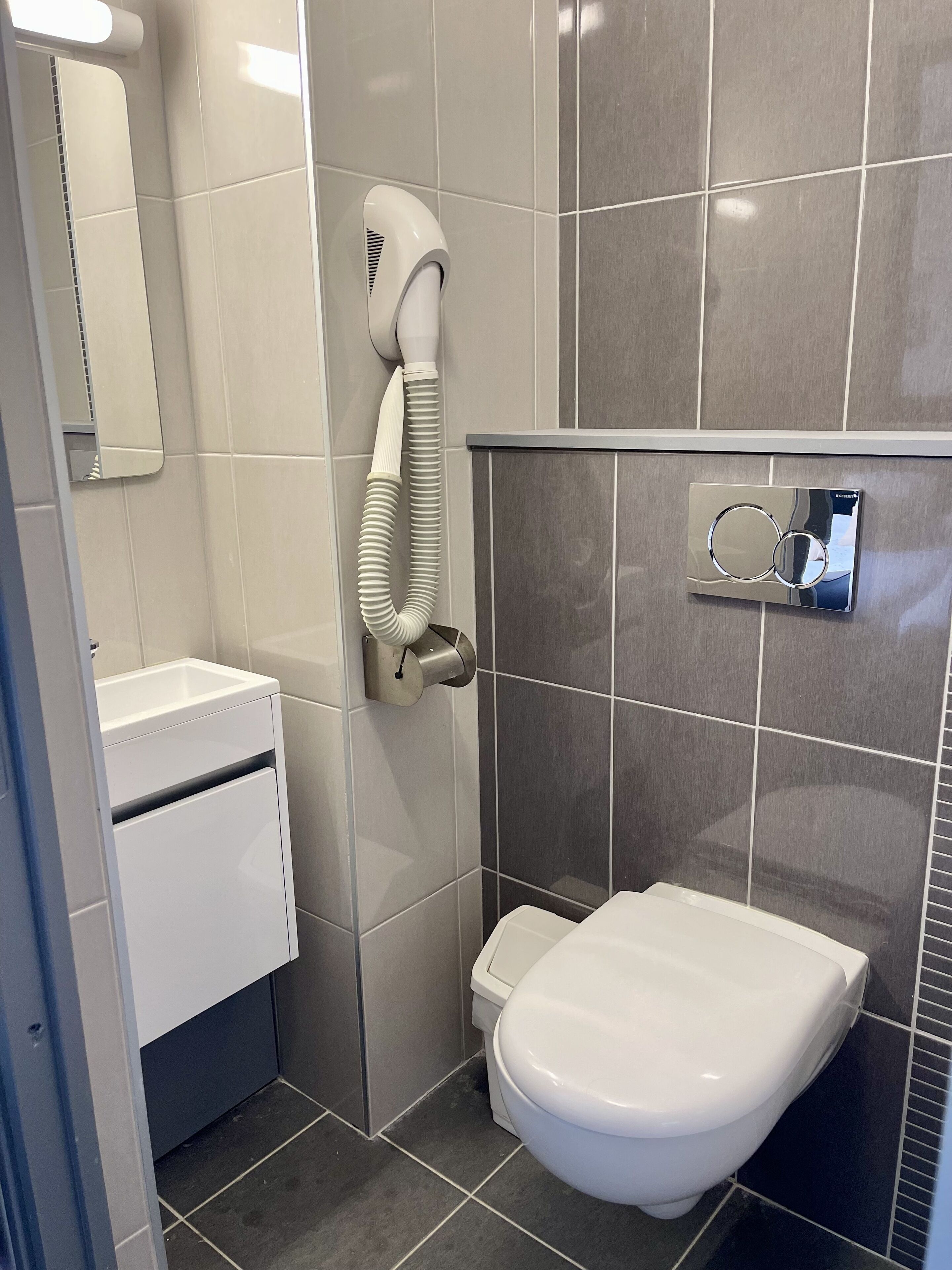 Un baño con inodoro, secamanos y dispensador de toallas.