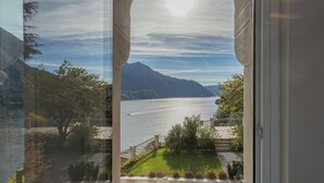 A view through an arched window of a lake with mountains in the background, a well-maintained lawn, and a fence. - Villa Moltrasio - Four Bedroom Villa, Sleeps 8 (Moltrasio)