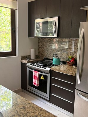 A kitchen with dark cabinets, a gas stove, a microwave, and a stainless steel refrigerator.