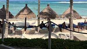 Ein Strand mit Palmen, Strohdächern und Liegestühlen.