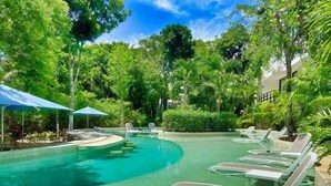 Ein Swimmingpool mit Liegestühlen und Sonnenschirmen, umgeben von üppiger Vegetation.