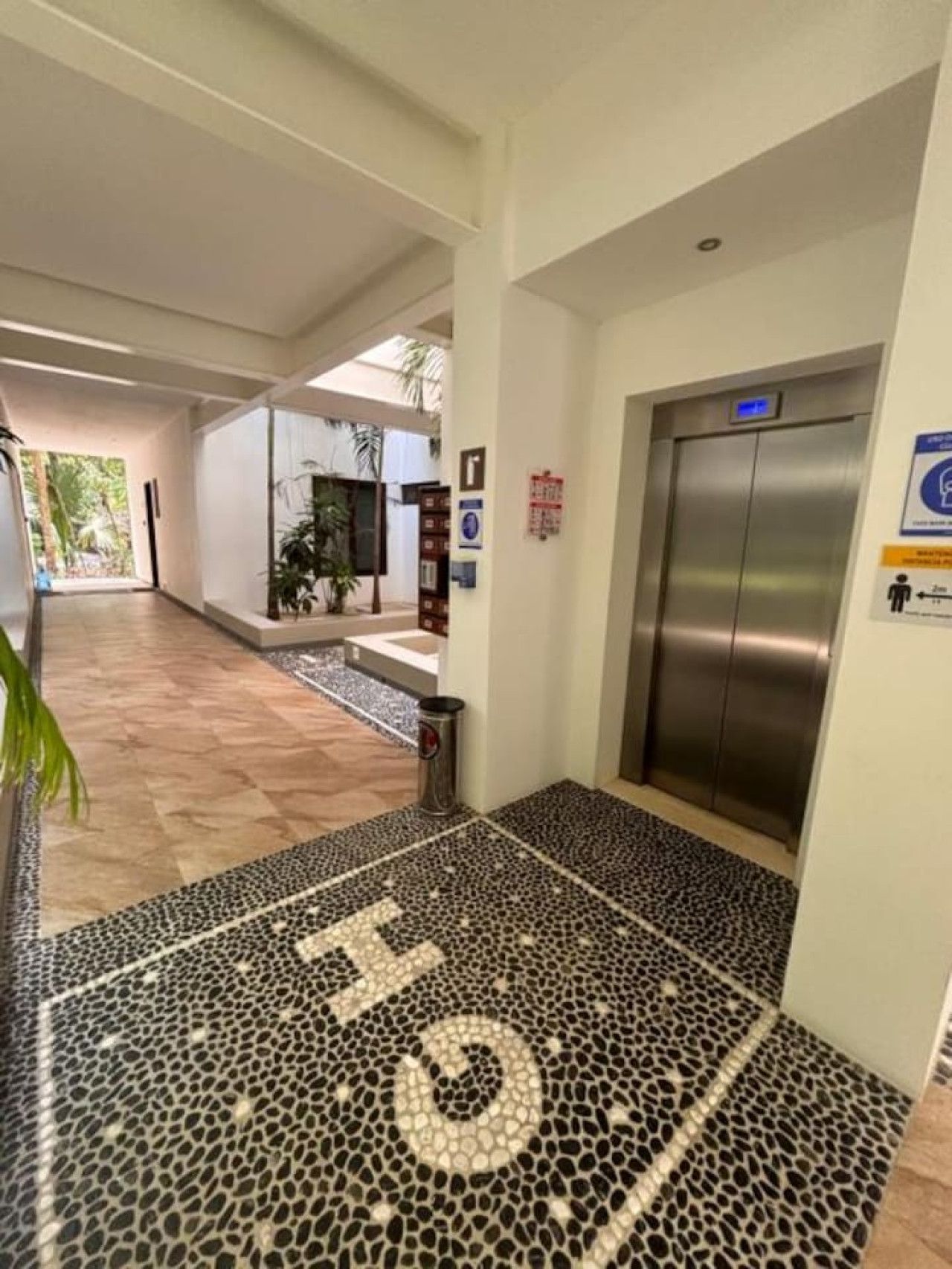 Un hall d’entrée moderne, avec un sol à motifs, qui mène à un ascenseur, un comptoir de réception et offre une vue sur l’extérieur.