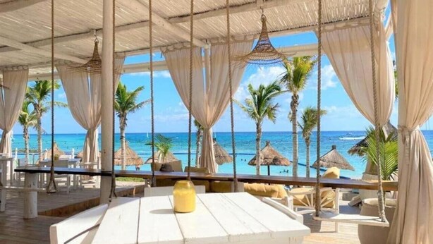 Ein Restaurant direkt am Strand mit Außenplätzen, Palmen und Meerblick.