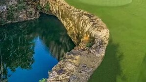 Ein Golfplatz mit Wasserhindernis und dichter Baumlandschaft im Hintergrund.