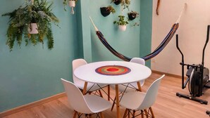 A room with a round table, four white chairs, a hammock, and several hanging plants.