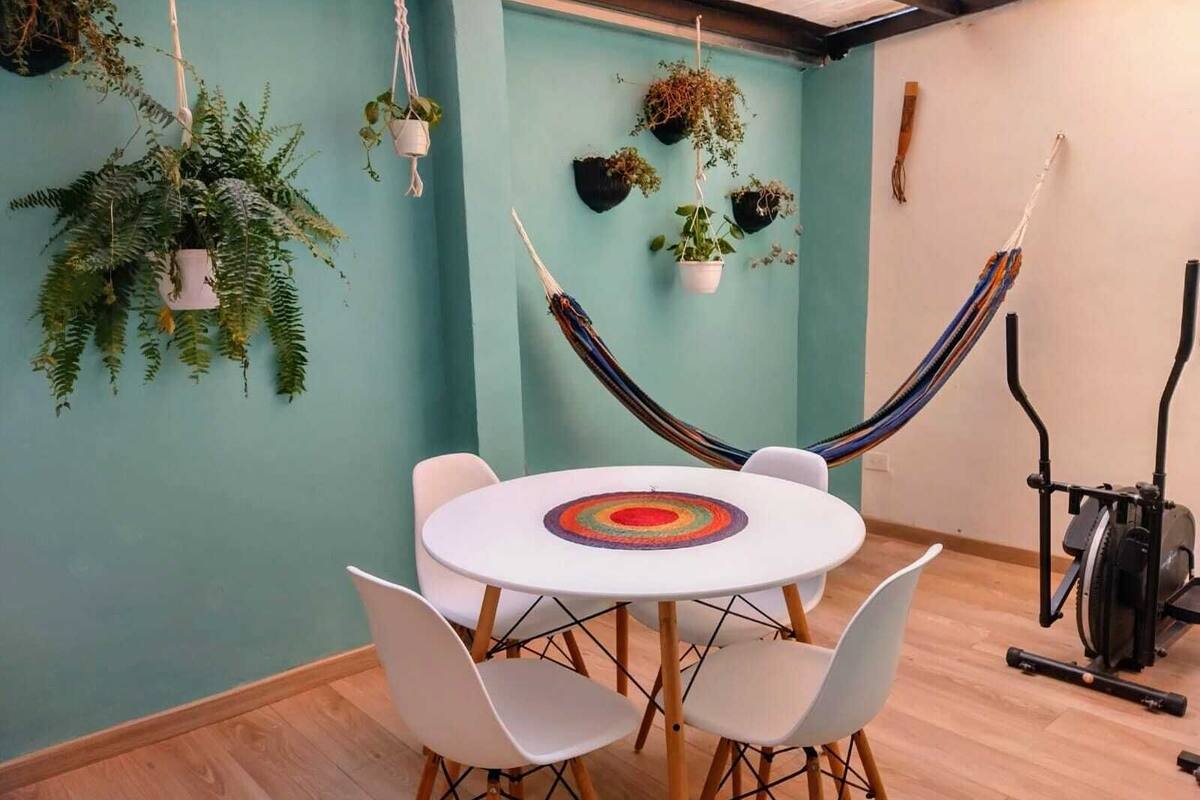 Ein Zimmer mit einem runden Tisch, vier weißen Stühlen, einer Hängematte und zahlreichen hängenden Pflanzen.